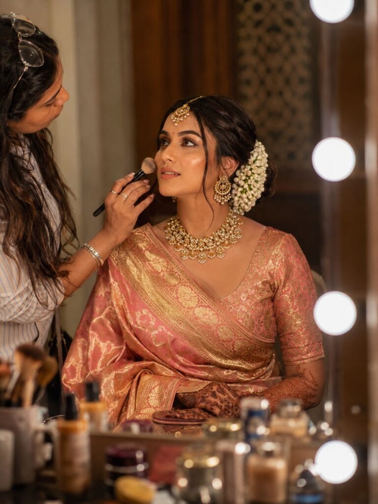 Indian bride getting bridal makeup done while wearing luxurious Banarasi saree.